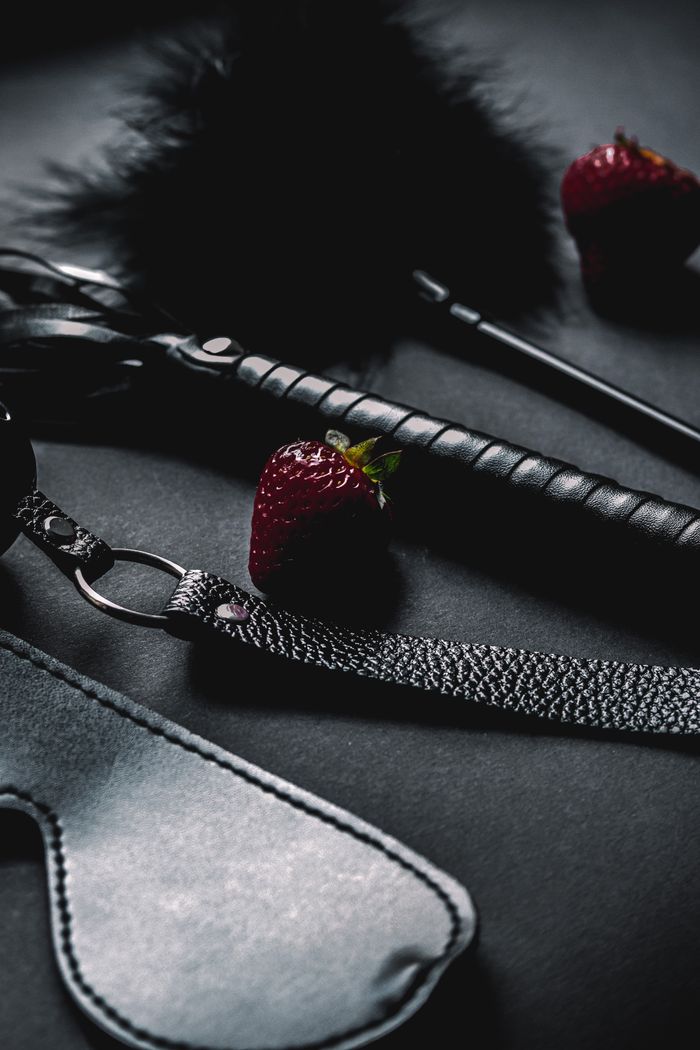 Close-up of intimate accessories and strawberries on a dark surface, creating a moody vibe.