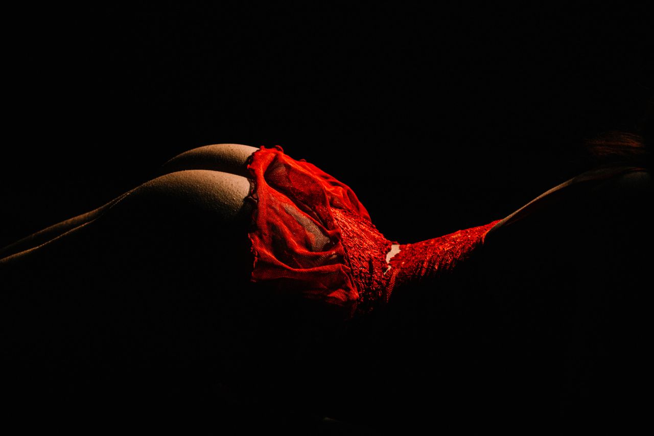 Striking studio shot of a woman posing in red lingerie against a dark background.